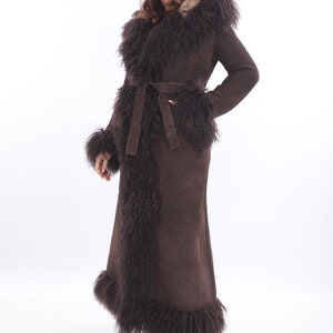 May include: A long brown suede coat with a natural fur collar and trim. The coat has a belt and is lined with a brown faux fur.