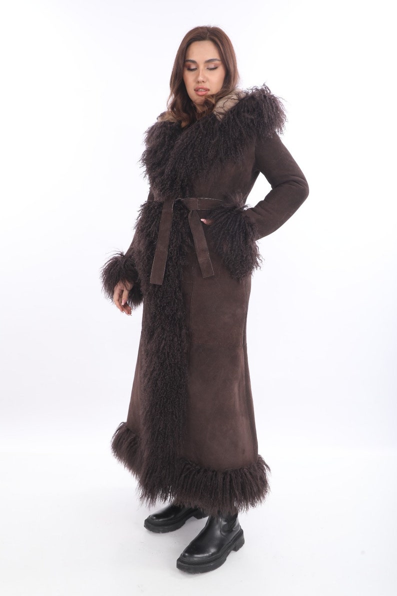 May include: A long brown suede coat with a natural fur collar and trim. The coat has a belt and is lined with a brown faux fur.