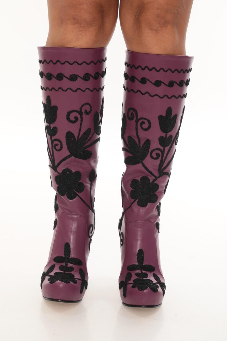 Puede incluir: Botas hasta la rodilla en color morado ciruela intenso con intrincados bordados negros. El dise&ntilde;o incluye motivos florales y patrones de remolinos que se extienden desde la punta hasta la parte superior de la ca&ntilde;a, con l&iacute;neas onduladas.