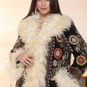 May include: A brown coat with a cream-colored, fluffy collar and cuffs. The coat features colorful floral embroidery and a velvet texture. The coat is a statement piece, perfect for adding a touch of bohemian flair to any outfit.