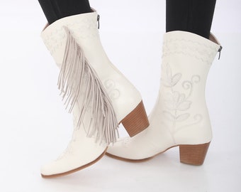 Peut inclure: Bottines de cow-boy en cuir blanc avec des motifs floraux brodés. Une botte a un détail de frange.