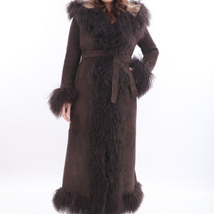 May include: A long brown suede coat with a fur collar and trim. The coat has a belt and a hood.
