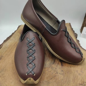 May include: A pair of brown leather shoes with black leather lacing. The shoes have a pointed toe and a flat sole.