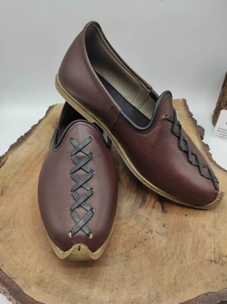 May include: A pair of brown leather shoes with black leather lacing. The shoes have a pointed toe and a flat sole.
