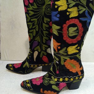 May include: A pair of black suede boots with colorful floral embroidery. The boots have a pointed toe and a block heel.