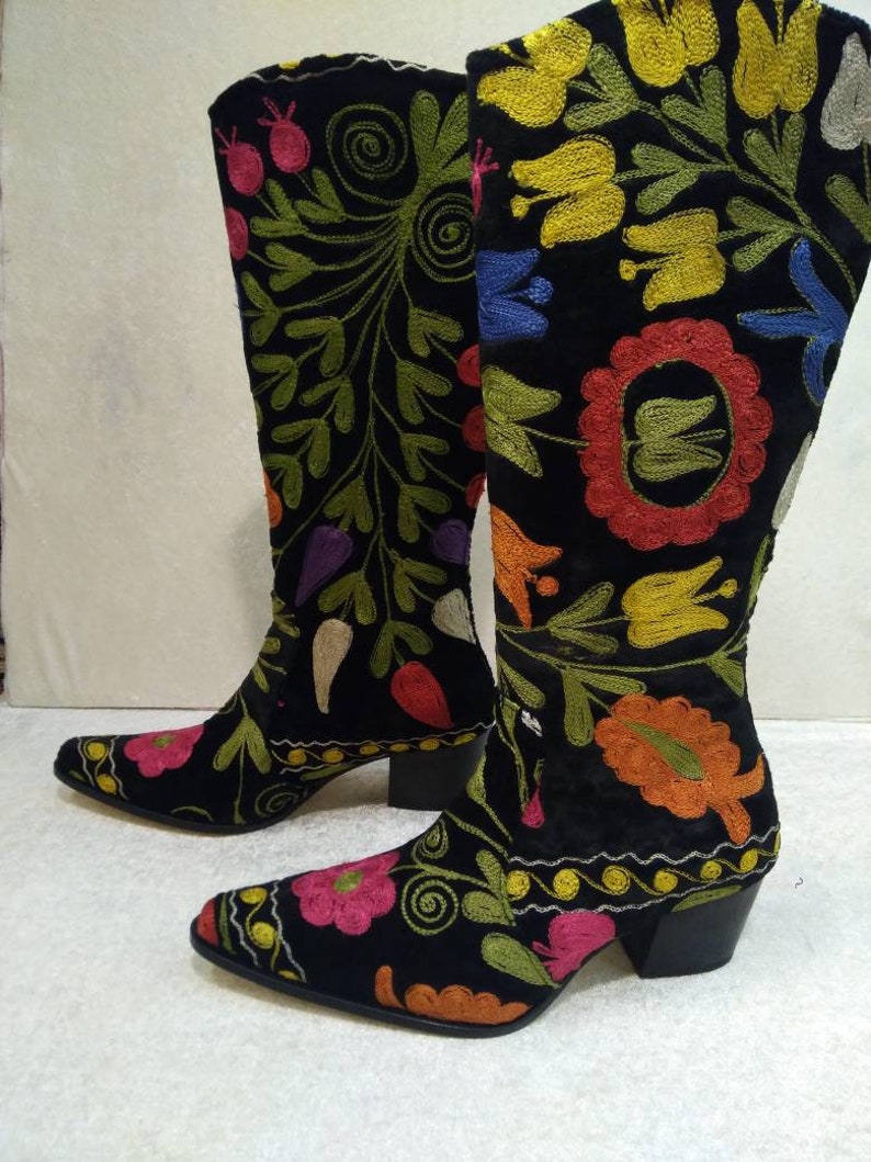 May include: A pair of black suede boots with colorful floral embroidery. The boots have a pointed toe and a block heel.