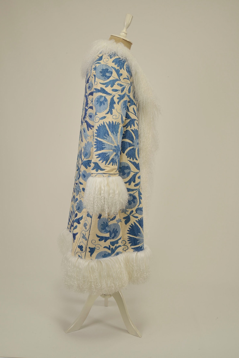 May include: A long white coat with a blue floral pattern and white fur trim around the collar, cuffs, and hem.