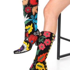 May include: A pair of black suede boots with colorful floral embroidery. The boots have a pointed toe and a low block heel.