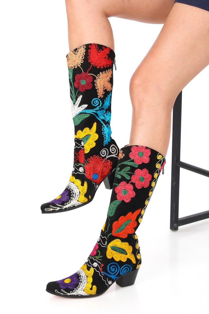 May include: A pair of black suede boots with colorful floral embroidery. The boots have a pointed toe and a low block heel.