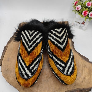Puede incluir: Un par de zapatillas de terciopelo con estampado en blanco y negro con ribete de piel negra. Las zapatillas tienen un patr&oacute;n amarillo en forma de chevron.