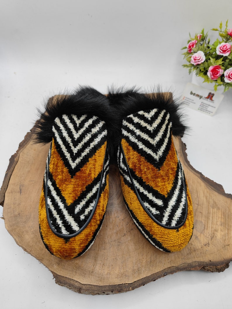 Puede incluir: Un par de zapatillas de terciopelo con estampado en blanco y negro con ribete de piel negra. Las zapatillas tienen un patr&oacute;n amarillo en forma de chevron.