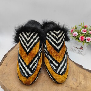Puede incluir: Un par de zapatillas de terciopelo a rayas blancas y negras con un patr&oacute;n de chevron amarillo y negro. Las zapatillas tienen un ribete de piel negra alrededor de la parte superior.