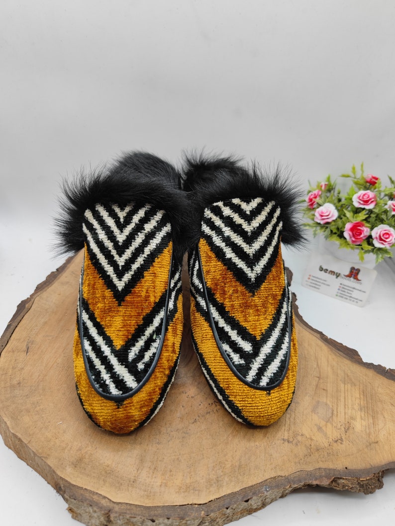 Puede incluir: Un par de zapatillas de terciopelo a rayas blancas y negras con un patr&oacute;n de chevron amarillo y negro. Las zapatillas tienen un ribete de piel negra alrededor de la parte superior.