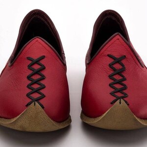 May include: A pair of red leather shoes with black stitching and a pointed toe. The shoes have a brown leather sole.