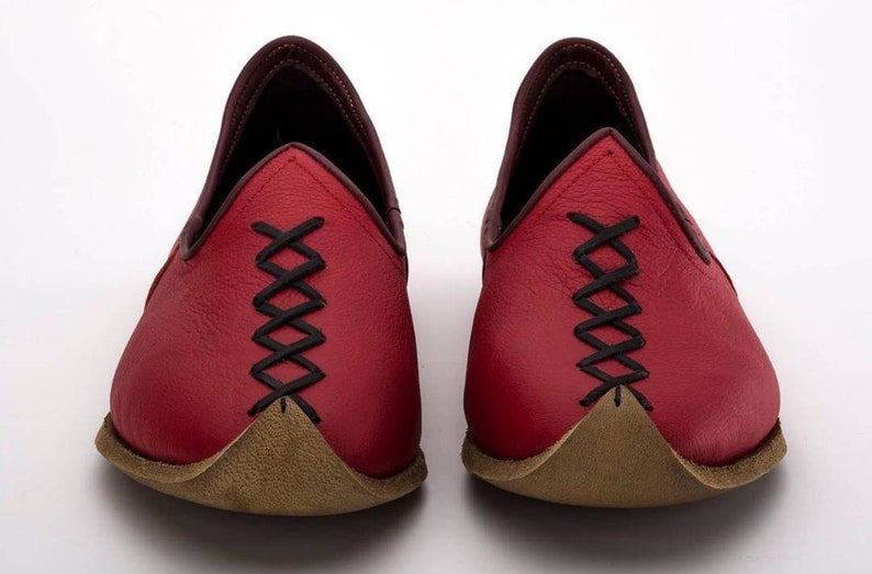 May include: A pair of red leather shoes with black stitching and a pointed toe. The shoes have a brown leather sole.