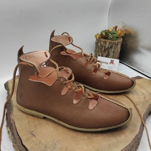 May include: A pair of brown leather sandals with laces that tie up the ankle. The sandals have a cut-out design and a flat sole.