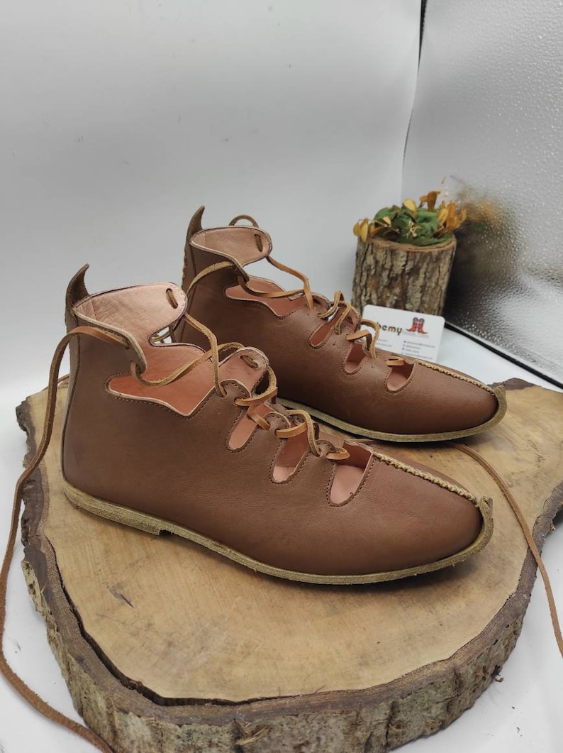 May include: A pair of brown leather sandals with laces that tie up the ankle. The sandals have a cut-out design and a flat sole.