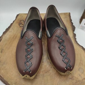 May include: A pair of brown leather shoes with black stitching. The shoes have a pointed toe and a slip-on design.
