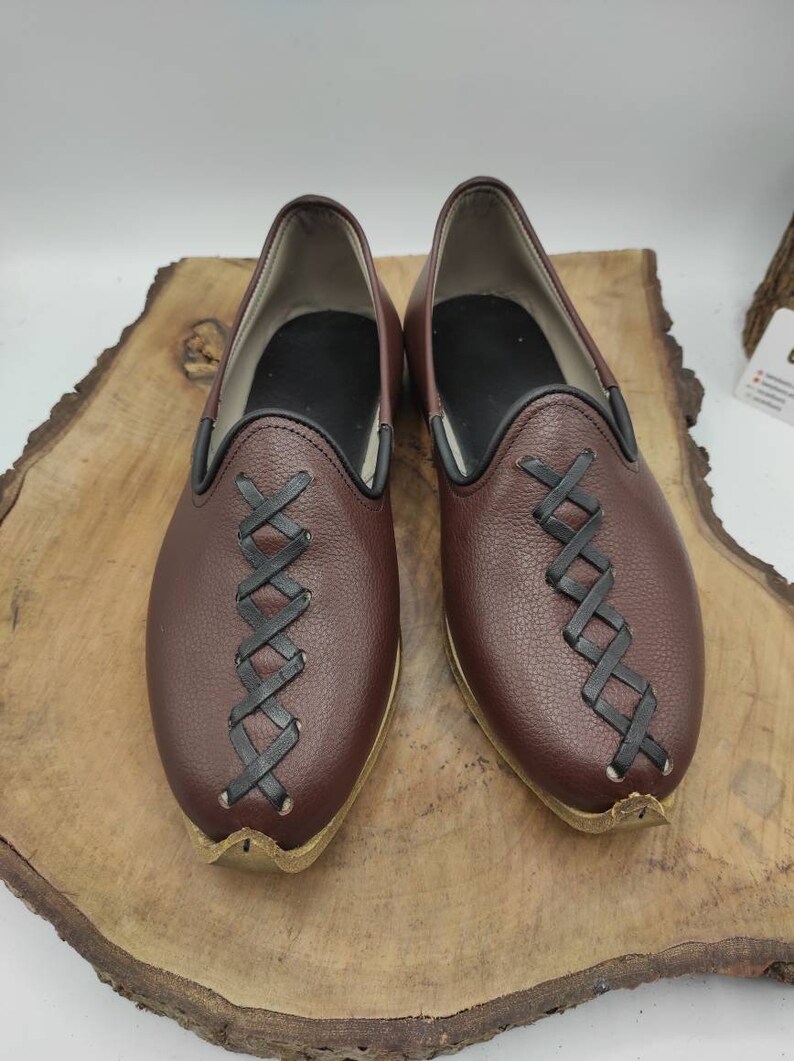 May include: A pair of brown leather shoes with black stitching. The shoes have a pointed toe and a slip-on design.
