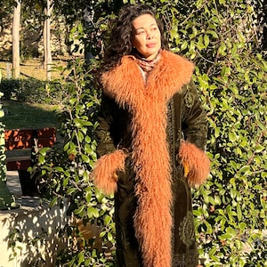 May include: A long, green velvet coat with a paisley pattern. The coat has a large, fluffy, peach-colored fur collar and cuffs.