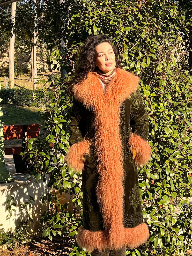 May include: A long, green velvet coat with a paisley pattern. The coat has a large, fluffy, peach-colored fur collar and cuffs.