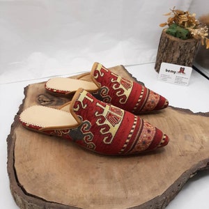 Puede incluir: Un par de zapatillas rojas y doradas con punta. Las zapatillas son de tela y tienen suela de cuero.