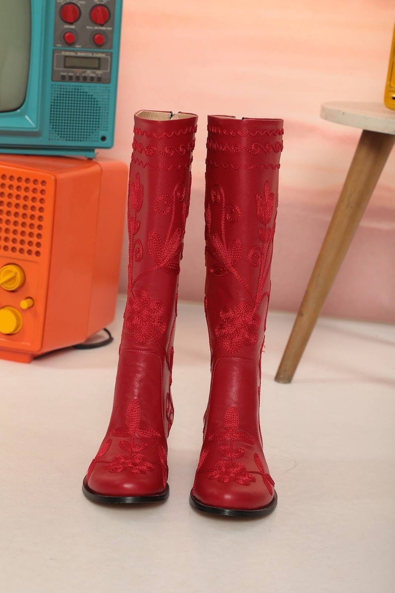 Puede incluir: Botas rojas hasta la rodilla con intrincado bordado floral. Las botas tienen punta y un tac&oacute;n peque&ntilde;o. El bordado es de un rojo m&aacute;s oscuro, creando un hermoso contraste. Las botas est&aacute;n hechas de un material liso similar al cuero.