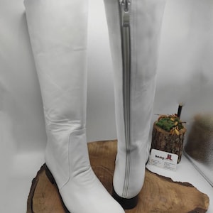 Puede incluir: Un par de botas blancas de cuero por encima de la rodilla con una cremallera en el interior de cada bota. Las botas tienen una punta puntiaguda y un tac&oacute;n bajo.
