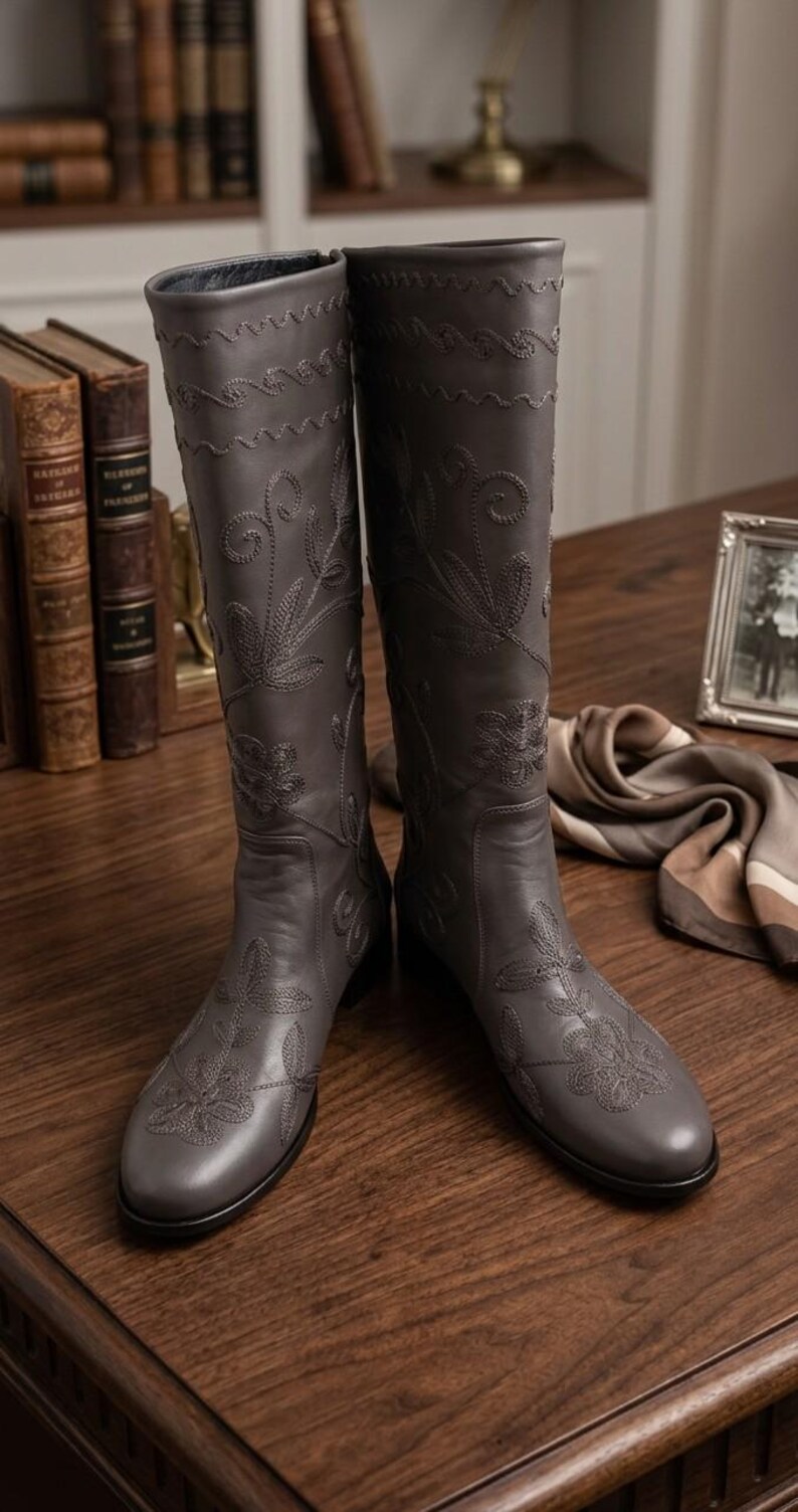 Puede incluir: Botas altas de cuero gris con intrincado bordado floral. Las botas tienen punta redonda y tac&oacute;n bajo. El dise&ntilde;o incluye costuras decorativas en el borde superior y en la parte delantera. Miden aproximadamente 40 cm de alto.