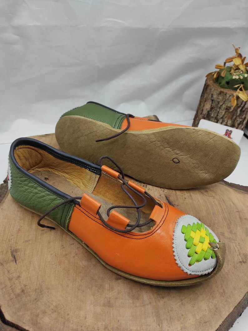 K&ouml;nnte beinhalten: Ein Paar orangefarbene und gr&uuml;ne Lederschuhe mit braunen Schn&uuml;rsenkeln. Die Schuhe haben ein dekoratives Design an der Spitze.