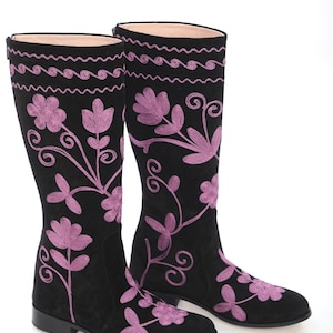 May include: A pair of black suede knee-high boots with pink floral embroidery. The boots have a low heel and a pointed toe.