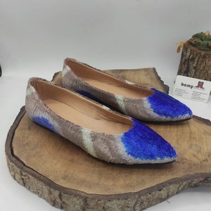May include: A pair of pointed-toe flats with a brown and white patterned fabric upper and blue velvet accents. The shoes are on a wooden surface.
