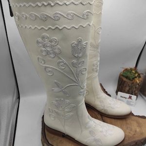 Pu&ograve; includere: Stivali bianchi in pelle con ricamo floreale bianco. Gli stivali hanno punta a punta e tacco basso.