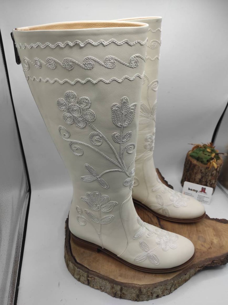 Pu&ograve; includere: Stivali bianchi in pelle con ricamo floreale bianco. Gli stivali hanno punta a punta e tacco basso.