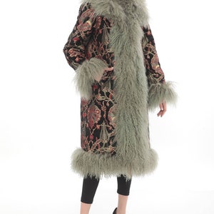 May include: A long black coat with a floral pattern and a green fur trim. The coat has a collar and cuffs made of the same fur.