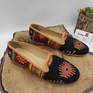 May include: A pair of black and red patterned women's loafers with a tan leather trim. The loafers have a geometric pattern with a red, yellow, and blue design.
