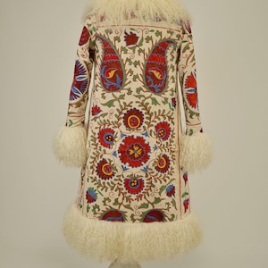 May include: A white coat with a long, fur-trimmed collar and cuffs. The coat is embroidered with a colorful floral pattern.