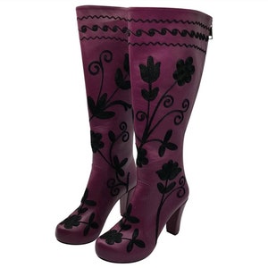 Puede incluir: Un par de botas moradas hasta la rodilla con bordados florales negros y un patr&oacute;n de l&iacute;neas onduladas cerca de la parte superior. Las botas tienen tac&oacute;n de bloque y punta redondeada. El texto BeMyBoots es visible arriba y abajo.
