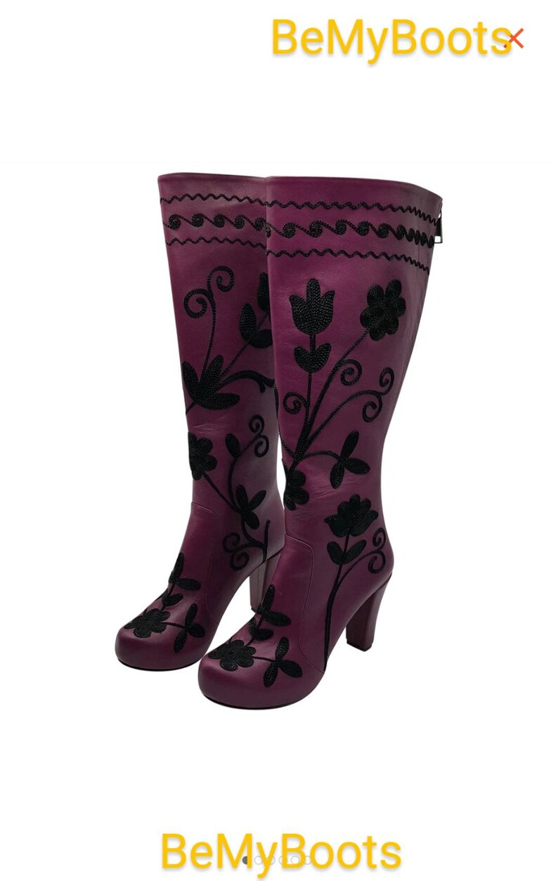 Puede incluir: Un par de botas moradas hasta la rodilla con bordados florales negros y un patr&oacute;n de l&iacute;neas onduladas cerca de la parte superior. Las botas tienen tac&oacute;n de bloque y punta redondeada. El texto BeMyBoots es visible arriba y abajo.
