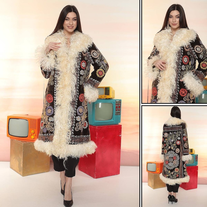 May include: A long, dark brown coat with colorful floral embroidery and a cream-colored, fluffy trim. The coat features a wide collar and cuffs with the same fluffy material. The coat is worn over black pants and heels.