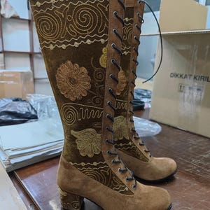 May include: Brown suede knee-high boots with a lace-up front and embroidered floral designs. The boots have a block heel and a side zipper.