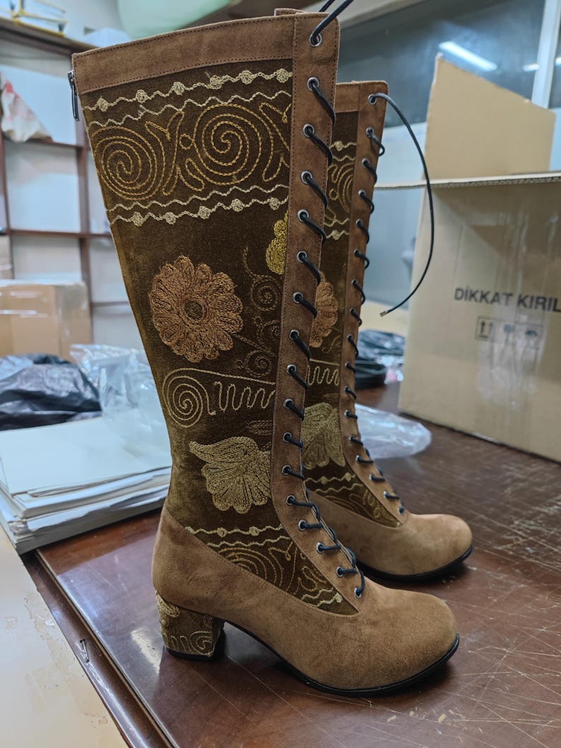May include: Brown suede knee-high boots with a lace-up front and embroidered floral designs. The boots have a block heel and a side zipper.
