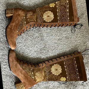 May include: A pair of brown suede knee-high boots with gold embroidery and lace-up closures. The boots have a block heel.