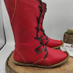 May include: Red leather boots with black laces and yellow stitching. The boots have a pointed toe and a flat sole.