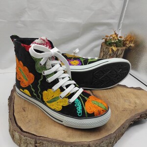 May include: Black high-top canvas shoes with colorful embroidered flowers. The shoes have white laces and a white rubber sole.