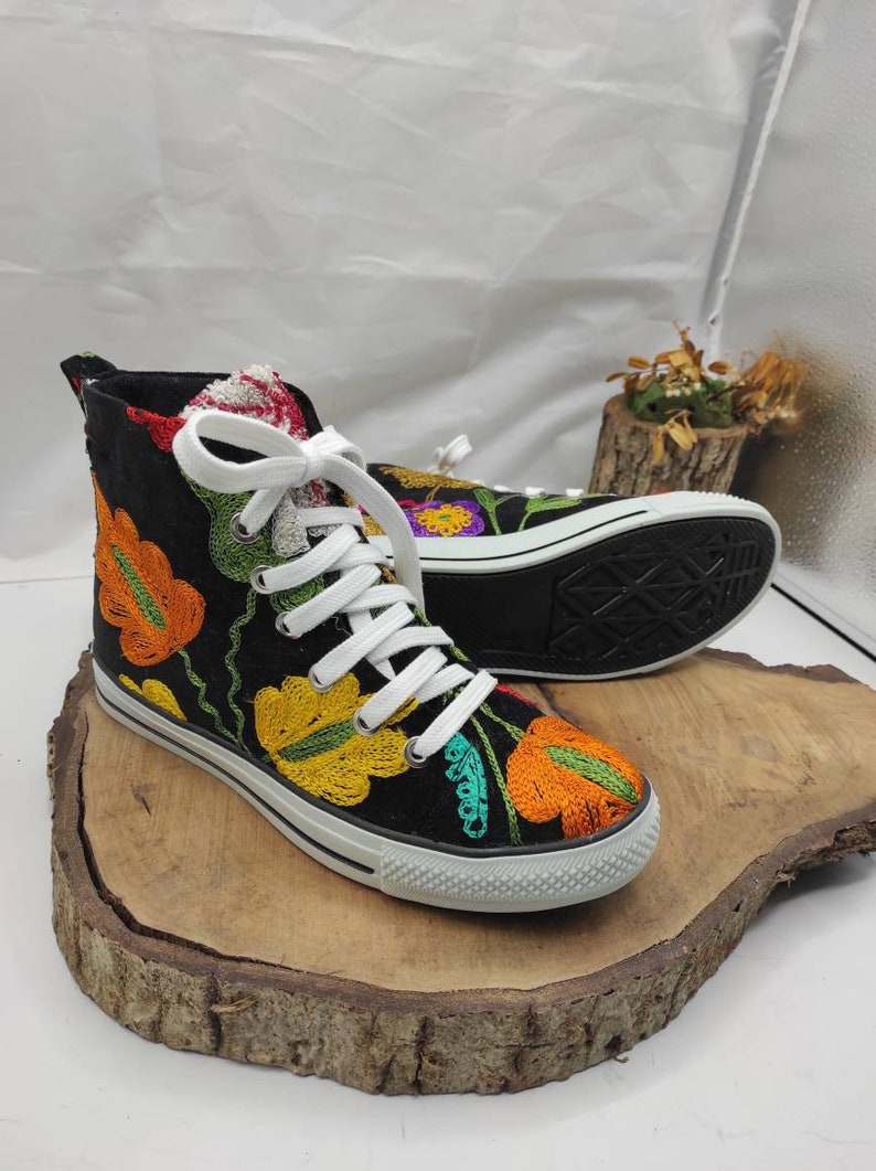 May include: Black high-top canvas shoes with colorful embroidered flowers. The shoes have white laces and a white rubber sole.