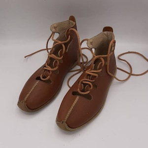 May include: A pair of brown leather sandals with laces. The sandals have a pointed toe and are tied up the ankle.