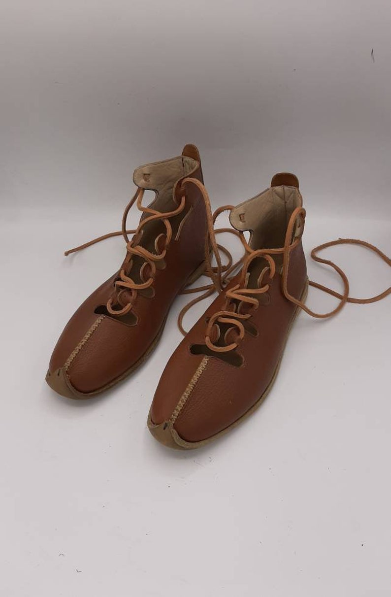 May include: A pair of brown leather sandals with laces. The sandals have a pointed toe and are tied up the ankle.