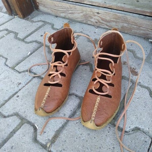 May include: A pair of brown leather sandals with laces. The sandals have a pointed toe and are tied up the ankle.
