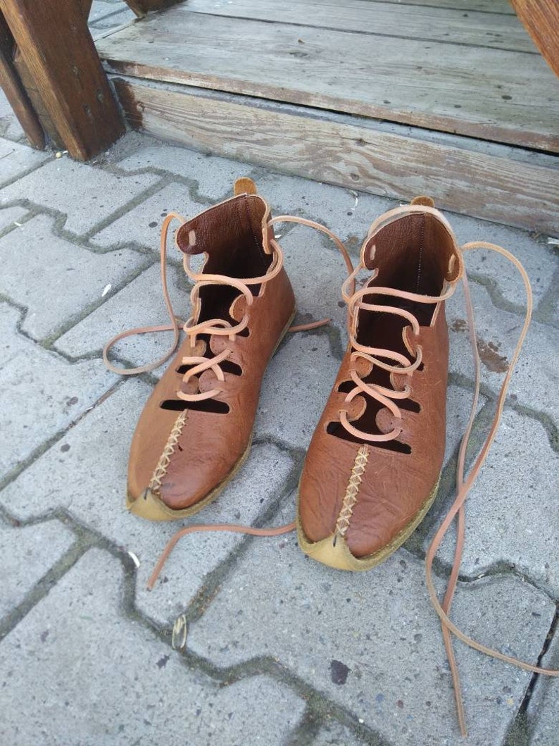 May include: A pair of brown leather sandals with laces. The sandals have a pointed toe and are tied up the ankle.